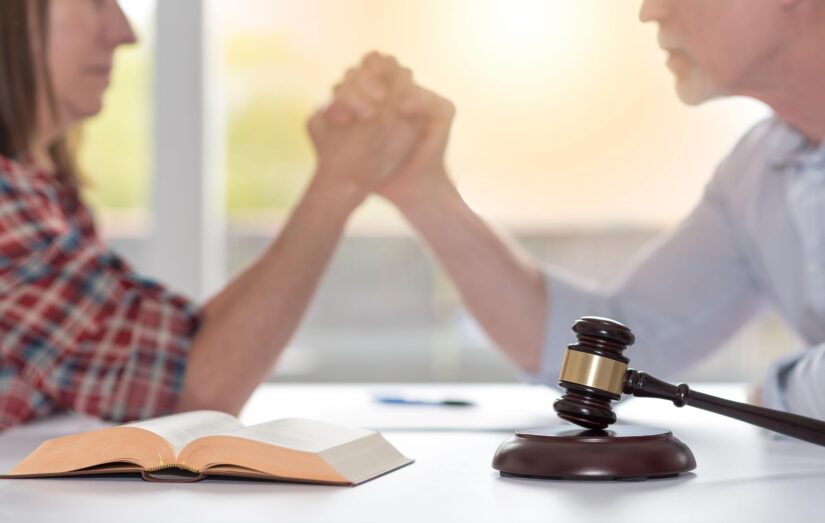 Judges Hammer With A Book On A Table While Couple Holding Hands In The Background