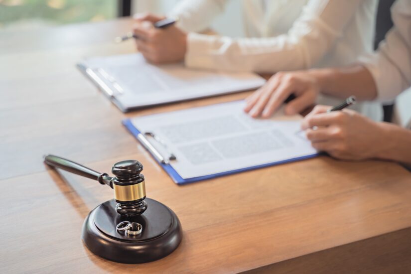 Judges Hammer With Two Rings On A Table While Two Person Signing Papers In the Backgroun